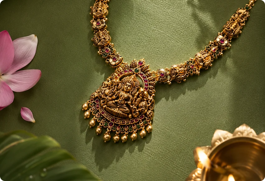 Ornate gold temple-style necklace displayed on green fabric with a diya lamp